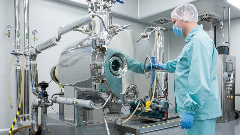 Biopharm worker wearing blue protection clothing, white head cover and and mask using equipment