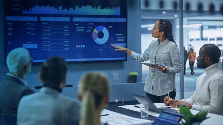 A group of 5 diverse employees look at a presentation of data being given.