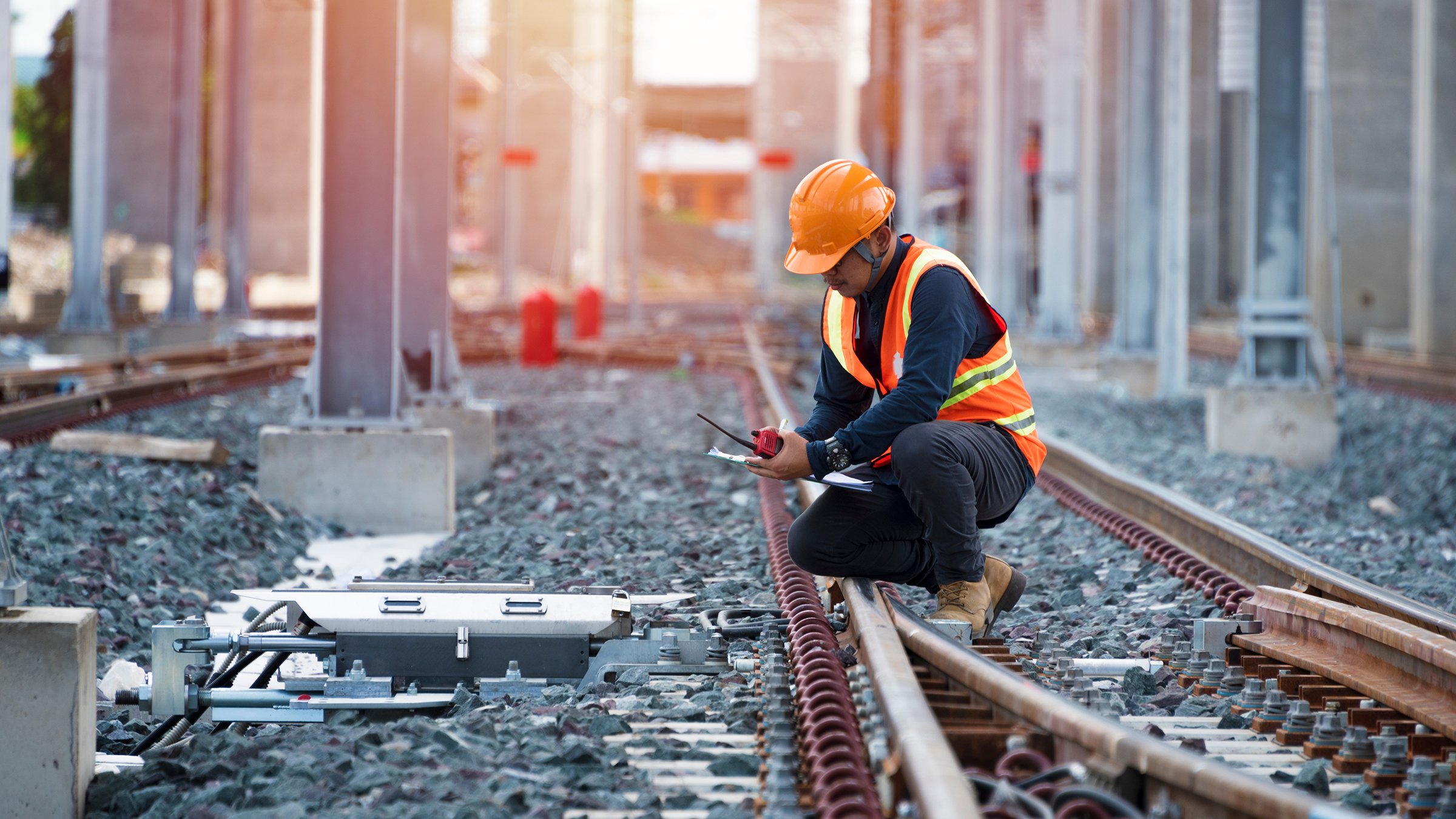 Male engineer in hard hat and high visibility vest sits on railway inspecting critical infrastructure