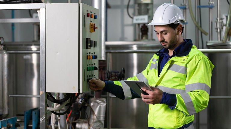 Ingeniero o trabajador de planta usando una computadora de tableta para averiguar cómo utilizar un panel de control de una máquina de la fábrica