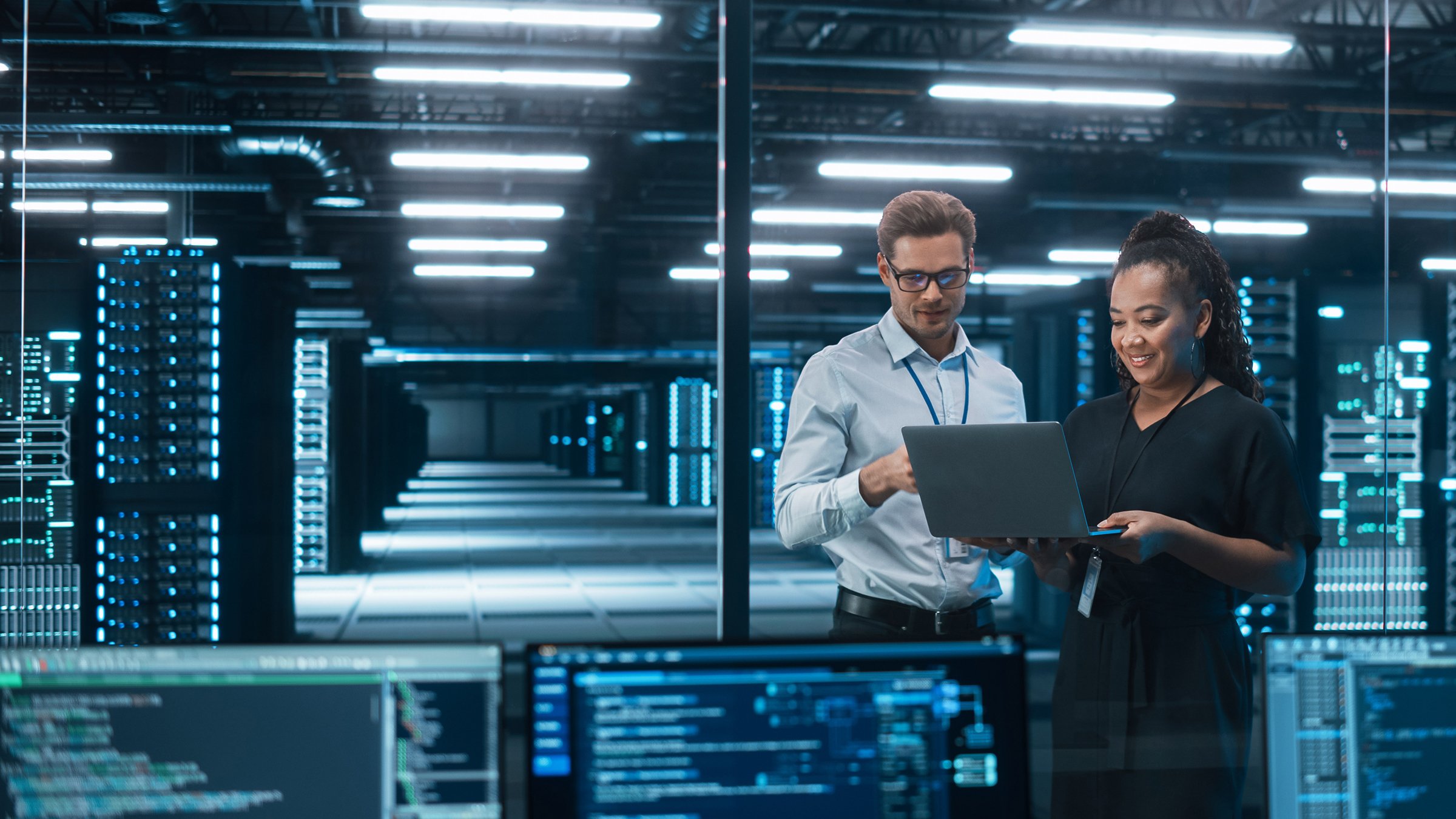 Two engineers one male and one female standing in an industrial security operations cetner holding a tablet monitoring cybersecurity network.