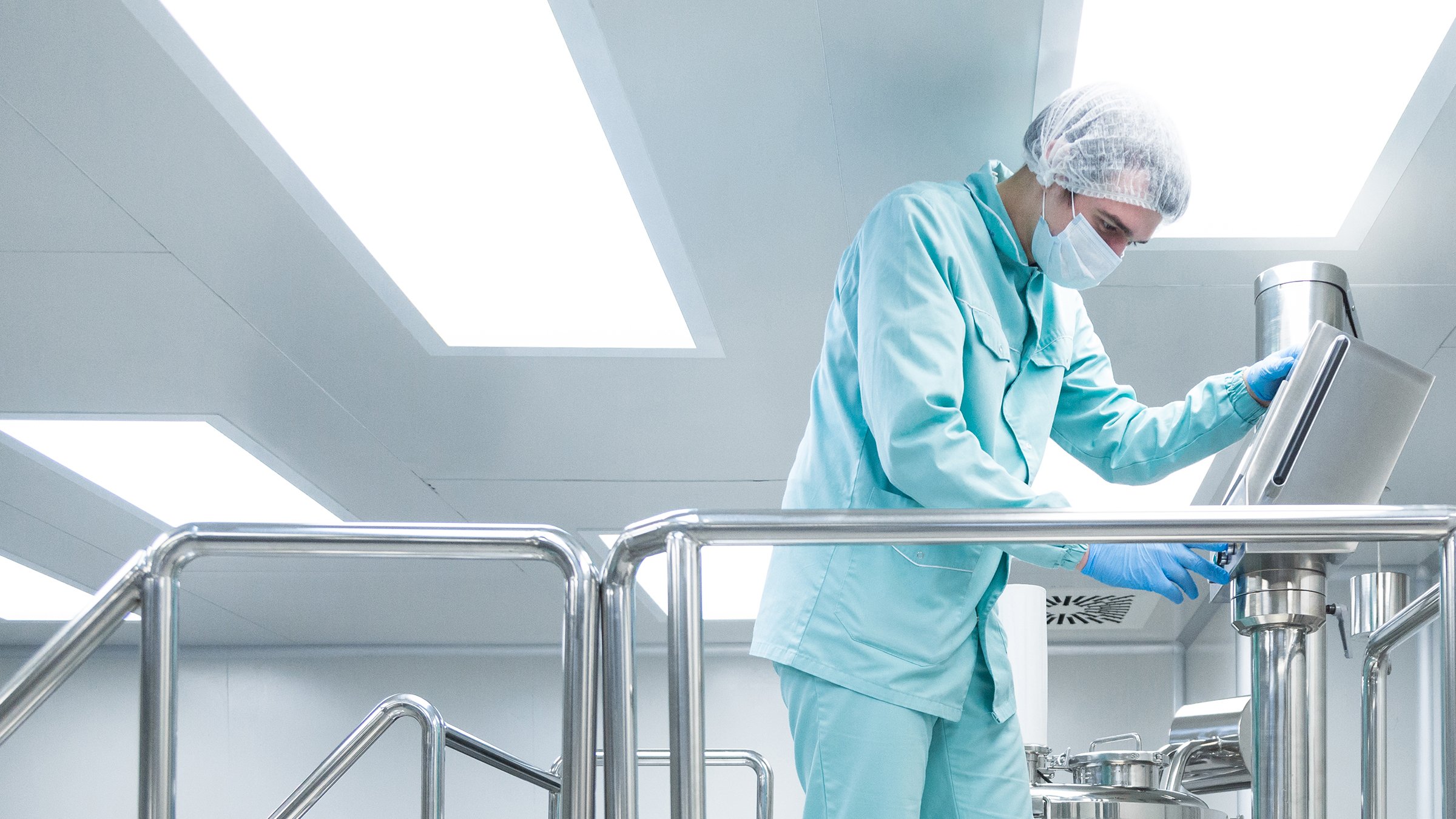 Un employé d’une usine pharmaceutique portant des vêtements de protection commande une ligne de production dans des conditions de travail stériles