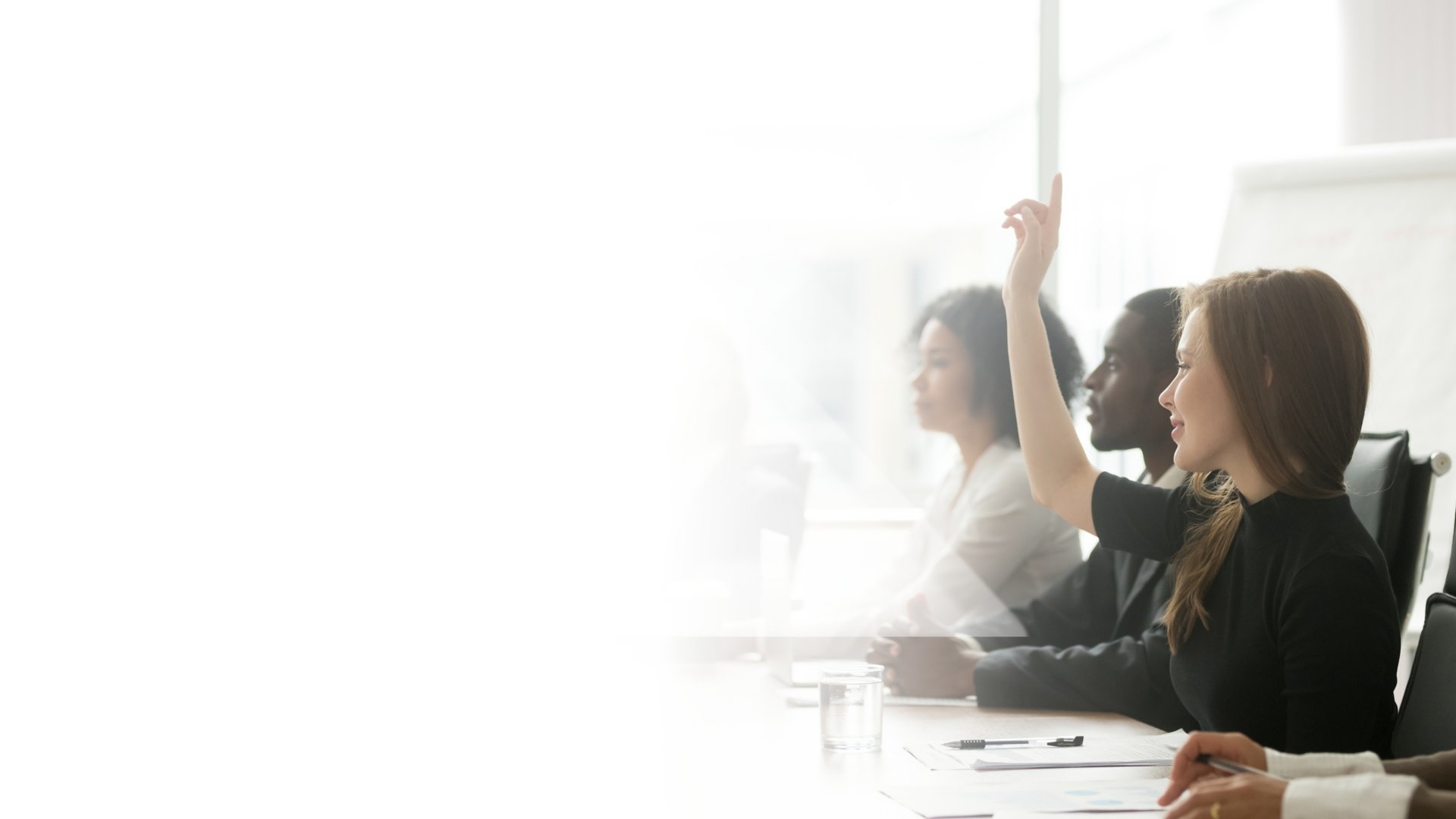Smiling and curious young businesswoman raising hand to ask questions in a multiracial corporate business training group meeting