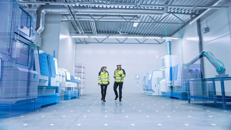 Dois engenheiros caminham pelo galpão da fábrica com modelos 3D de realidade aumentada da linha de produção de máquinas CNC. 