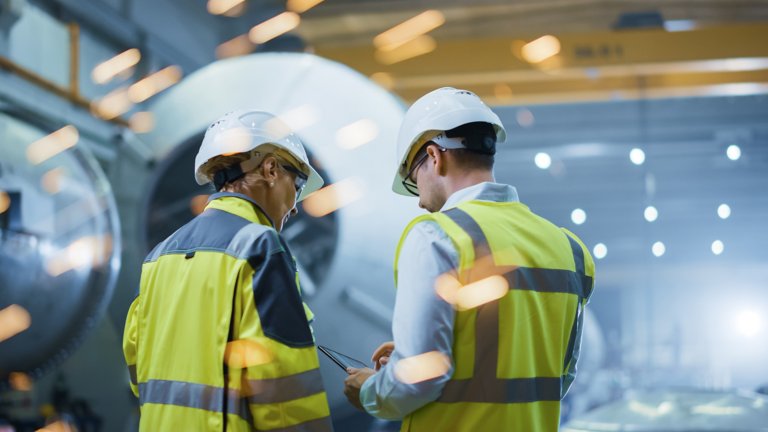 Two engineers using a tablet and standing in front of a oil and gas transport pipeline with sparks flying