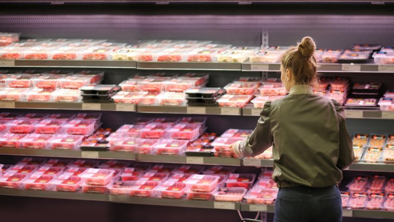 Une femme se tenant devant le rayon boucherie d'un magasin pour choisir une barquette.