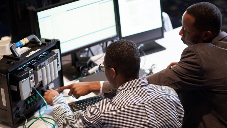 Two men in front of computers screens take Rockwell Automation e-learning course and point to ControlLogix Controller.