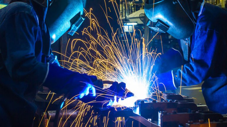 Two welders dressed in blue coveralls and face masks