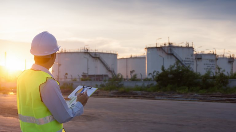 Engineer writing on the paper in front of the oil tank.Refinery, gas and oil