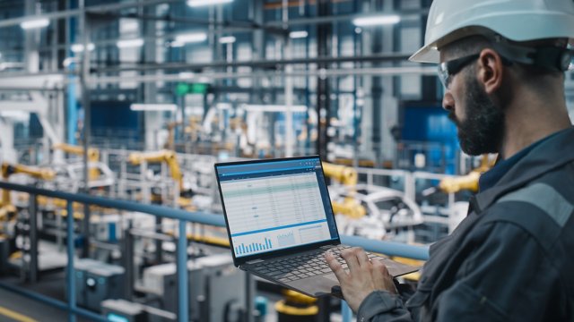 Engineer on a industrial plant floor holding a laptop requiring patch management solutions
