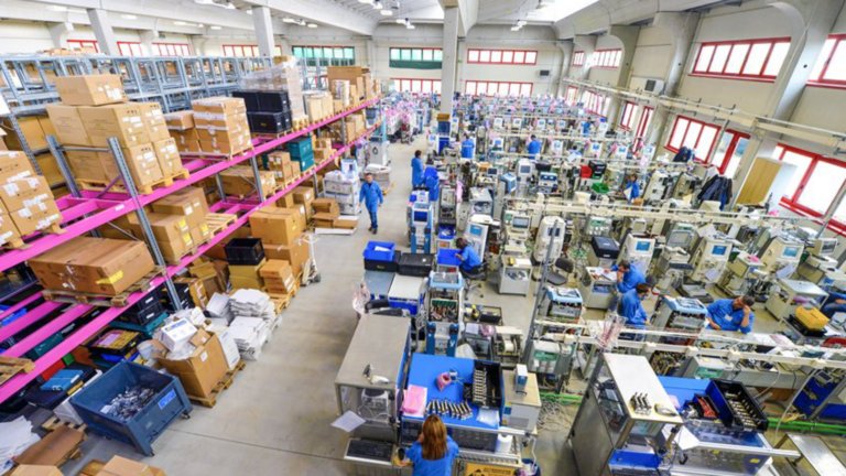 Life sciences workers move around a warehouse that contains medical devices waiting to be packaged and shelves stacked with large boxes.