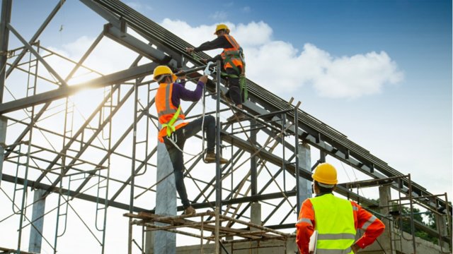 Two construction workers in neon vests working on outdoor construction site wiring structure