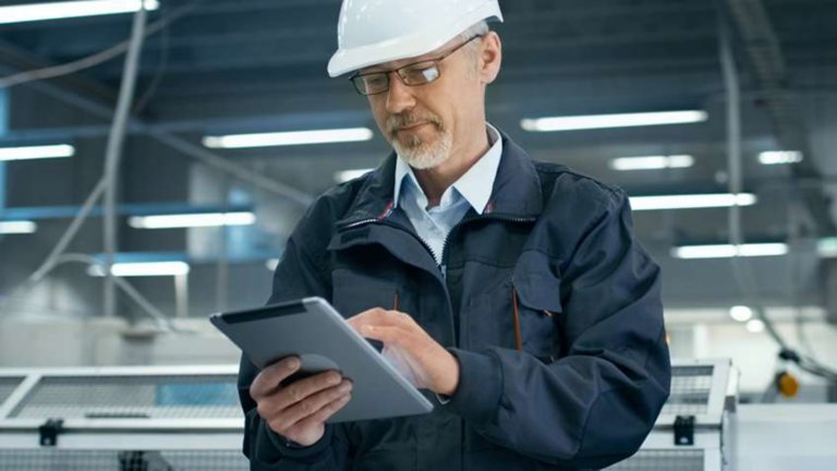 戴著白色安全帽的男員工正在工廠中將資料輸入到平板電腦上