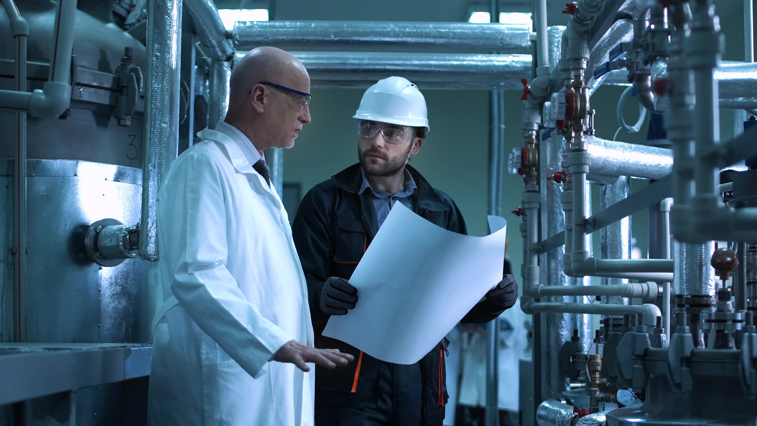 a male engineer in a hard hat talking to another man in a lab coat