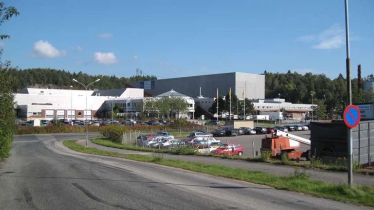 A curved road next to a parking lot filled with cars leads to an Oriola AB facility in the United Kingdom.